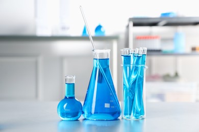 Photo of Different laboratory glassware with light blue liquid on table indoors
