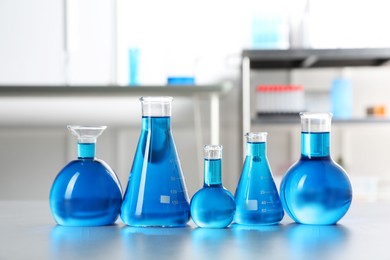 Photo of Different laboratory glassware with light blue liquid on table indoors