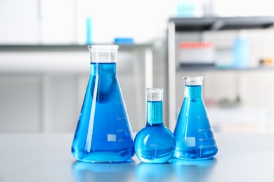 Photo of Flasks with light blue liquid on table in laboratory