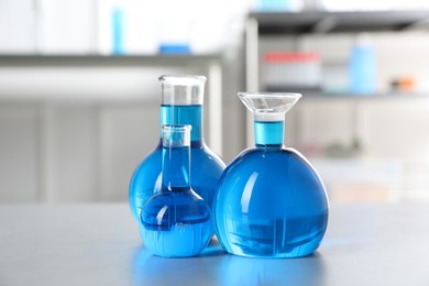 Photo of Flasks with light blue liquid on table in laboratory
