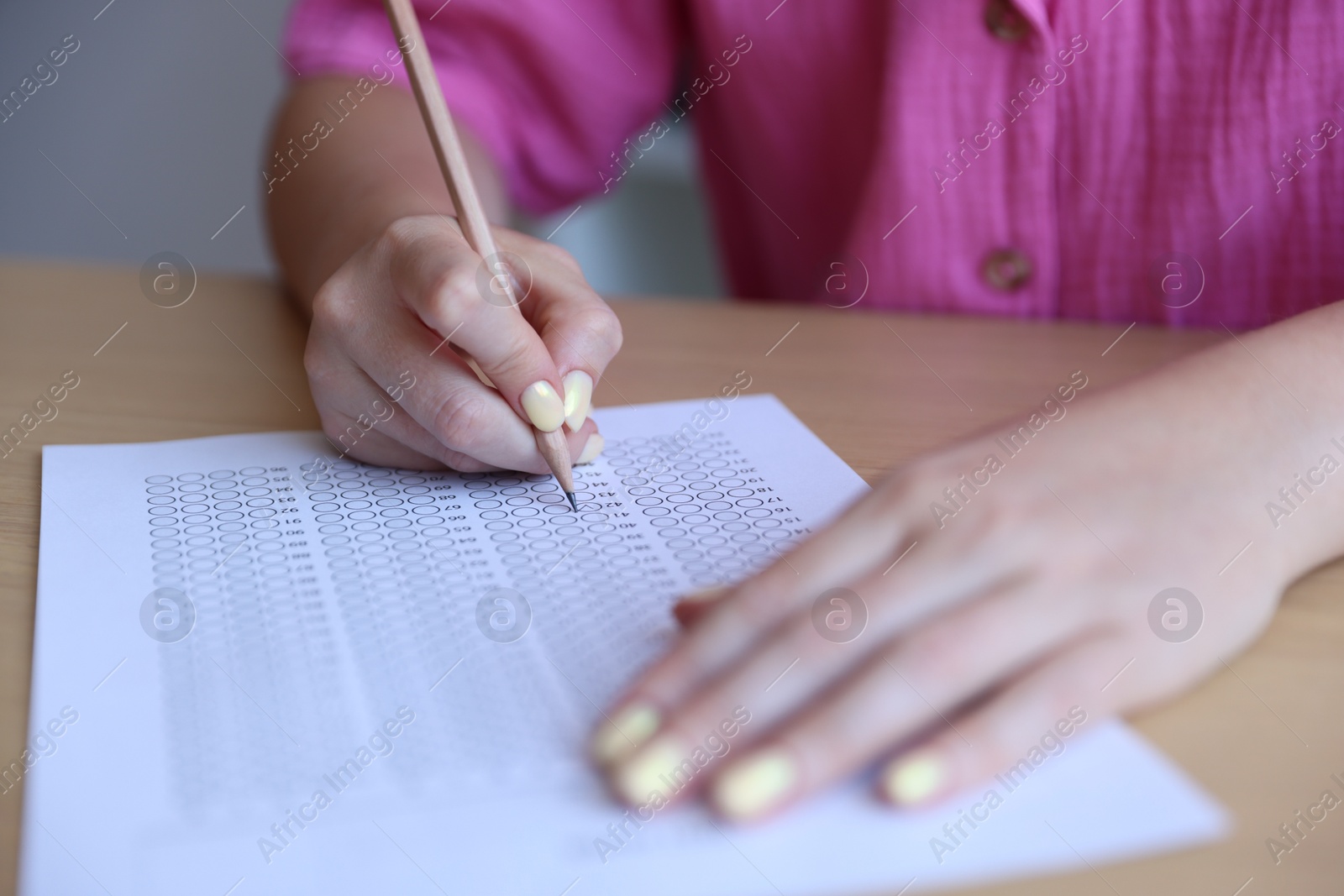 Photo of Student filling out multiple choice test at table in class, closeup. Passing exam