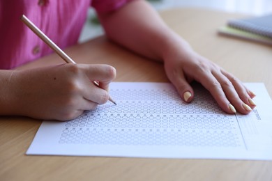Photo of Student filling out multiple choice test at wooden table, closeup. Passing exam