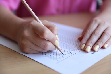 Photo of Student filling out multiple choice test at wooden table, closeup. Passing exam