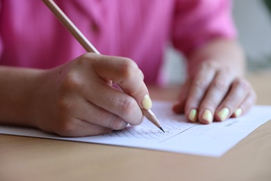 Photo of Student filling out multiple choice test at wooden table, closeup. Passing exam