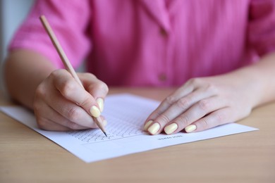 Photo of Student filling out multiple choice test at wooden table, closeup. Passing exam