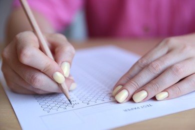 Photo of Student filling out multiple choice test at wooden table, closeup. Passing exam