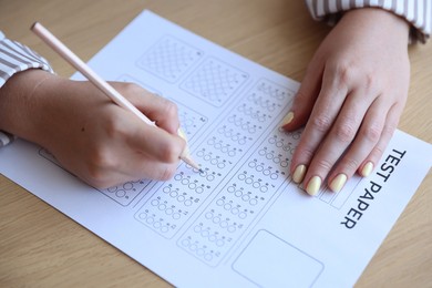 Photo of Student filling out multiple choice test at wooden table, closeup. Passing exam