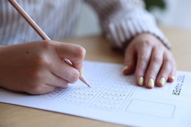 Photo of Student filling out multiple choice test at table in class, closeup. Passing exam