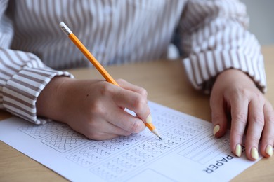 Photo of Student filling out multiple choice test at wooden table, closeup. Passing exam