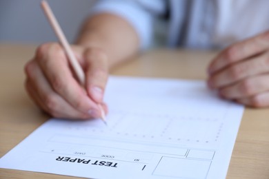 Photo of Student filling out multiple choice test at wooden table, closeup. Passing exam