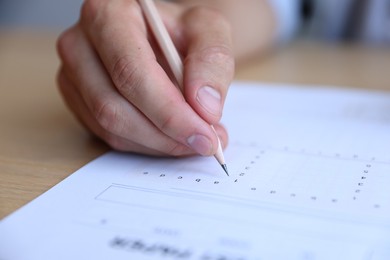 Photo of Student filling out multiple choice test at wooden table, closeup. Passing exam