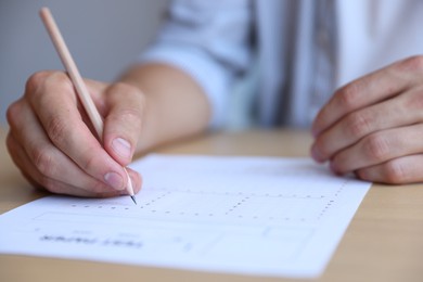 Photo of Student filling out multiple choice test at table in class, closeup. Passing exam