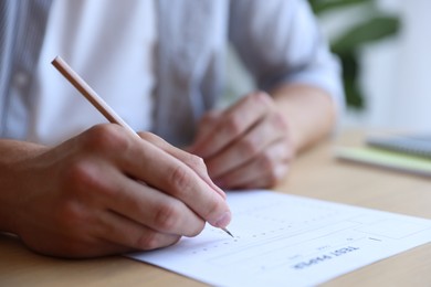 Photo of Student filling out multiple choice test at table in class, closeup. Passing exam