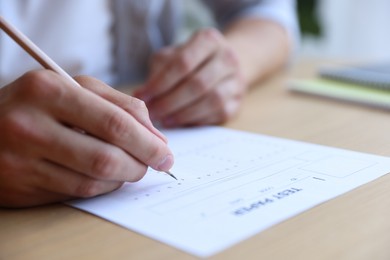 Photo of Student filling out multiple choice test at table in class, closeup. Passing exam