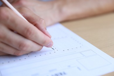 Photo of Student filling out multiple choice test at wooden table, closeup. Passing exam