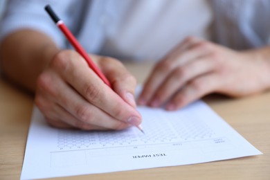 Photo of Student filling out multiple choice test at wooden table, closeup. Passing exam