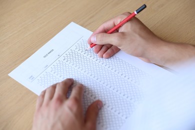Photo of Student filling out multiple choice test at wooden table, closeup. Passing exam