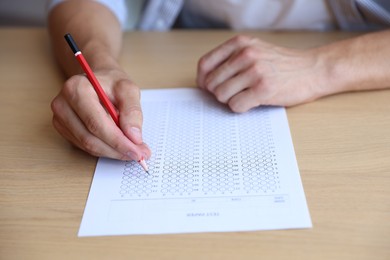 Photo of Student filling out multiple choice test at wooden table, closeup. Passing exam