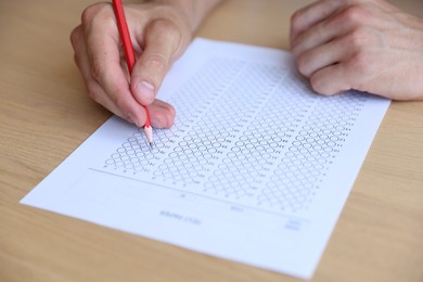 Photo of Student filling out multiple choice test at wooden table, closeup. Passing exam