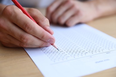 Photo of Student filling out multiple choice test at wooden table, closeup. Passing exam