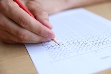 Photo of Student filling out multiple choice test at wooden table, closeup. Passing exam