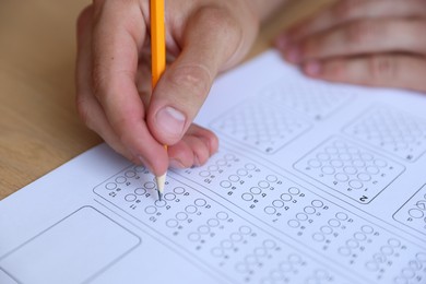 Photo of Student filling out multiple choice test at wooden table, closeup. Passing exam