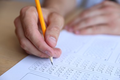 Photo of Student filling out multiple choice test at wooden table, closeup. Passing exam