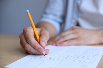 Photo of Student filling out multiple choice test at table in class, closeup. Passing exam