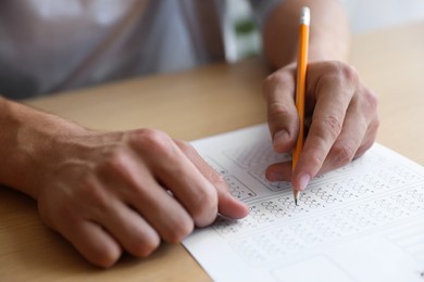 Photo of Student filling out multiple choice test at wooden table, closeup. Passing exam