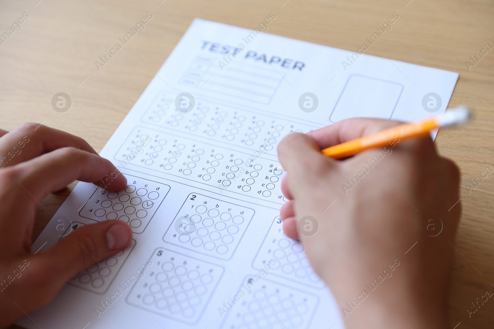 Student filling out multiple choice test at wooden table, closeup. Passing exam Photo of Student filling out multiple choice test at wooden table, closeup. Passing exam