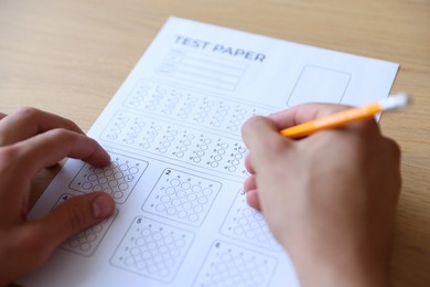 Photo of Student filling out multiple choice test at wooden table, closeup. Passing exam
