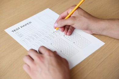 Photo of Student filling out multiple choice test at wooden table, closeup. Passing exam