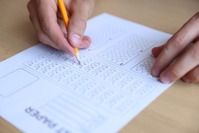 Photo of Student filling out multiple choice test at wooden table, closeup. Passing exam