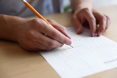 Photo of Student filling out multiple choice test at wooden table, closeup. Passing exam