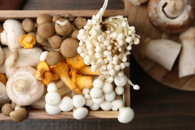 Photo of Different raw mushrooms and crate on wooden table, flat lay
