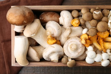 Photo of Different raw mushrooms in crate on wooden table, top view