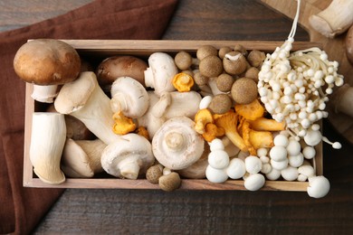 Photo of Different raw mushrooms and crate on wooden table, flat lay