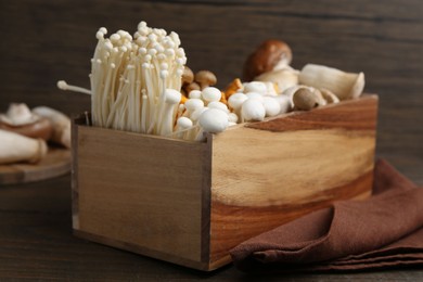 Photo of Different raw mushrooms in crate and napkin on wooden table, closeup