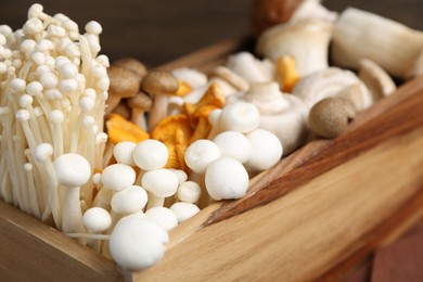 Photo of Different raw mushrooms in wooden crate on table, closeup