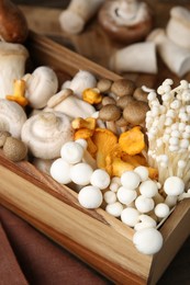 Photo of Different raw mushrooms in crate on table, closeup
