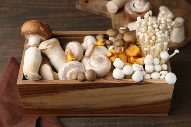 Photo of Different raw mushrooms in crate on wooden table, closeup