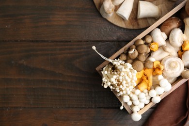 Photo of Different raw mushrooms and crate on wooden table, flat lay. Space for text