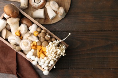 Photo of Different raw mushrooms and crate on wooden table, flat lay. Space for text