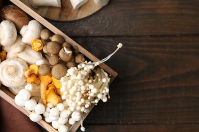 Photo of Different raw mushrooms in crate on wooden table, flat lay. Space for text