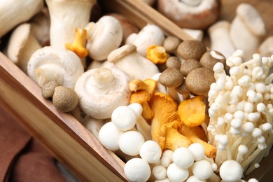 Photo of Different raw mushrooms in wooden crate on table, closeup