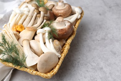 Photo of Different raw mushrooms and dill in wicker basket on grey textured table, closeup. Space for text