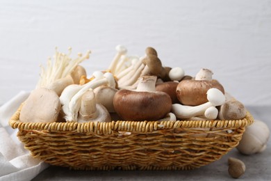Photo of Different raw mushrooms in wicker basket on grey textured table against light background, closeup