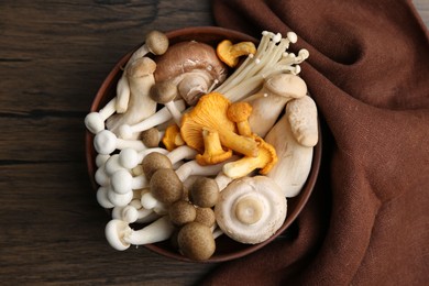 Photo of Different raw mushrooms in bowl on wooden table, top view