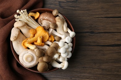 Photo of Different raw mushrooms in bowl on wooden table, top view. Space for text