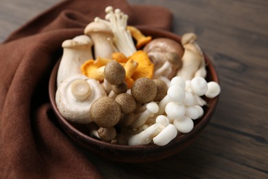 Photo of Different raw mushrooms in bowl on wooden table, closeup